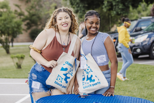 Two female students smiling holding 爱尤物Block Party bags