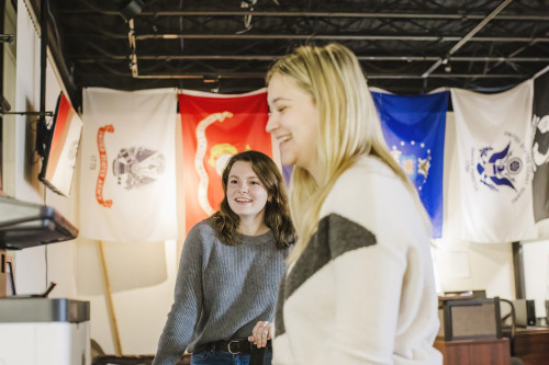 Two female students in the Haberman Center for Veterans, flags on wall in backround